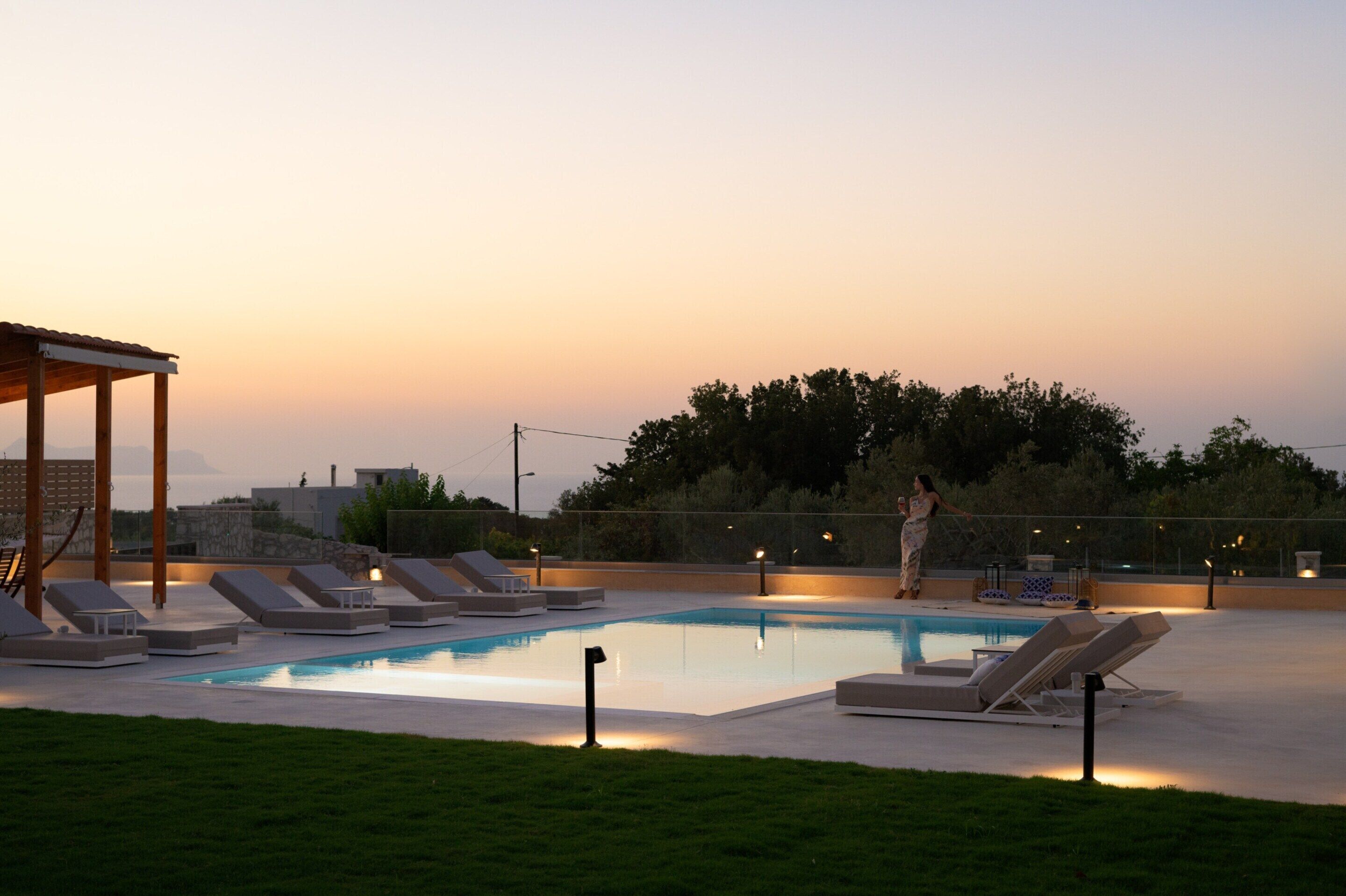 A swimming pool with lounge chairs, a covered area, and a view of trees and buildings.