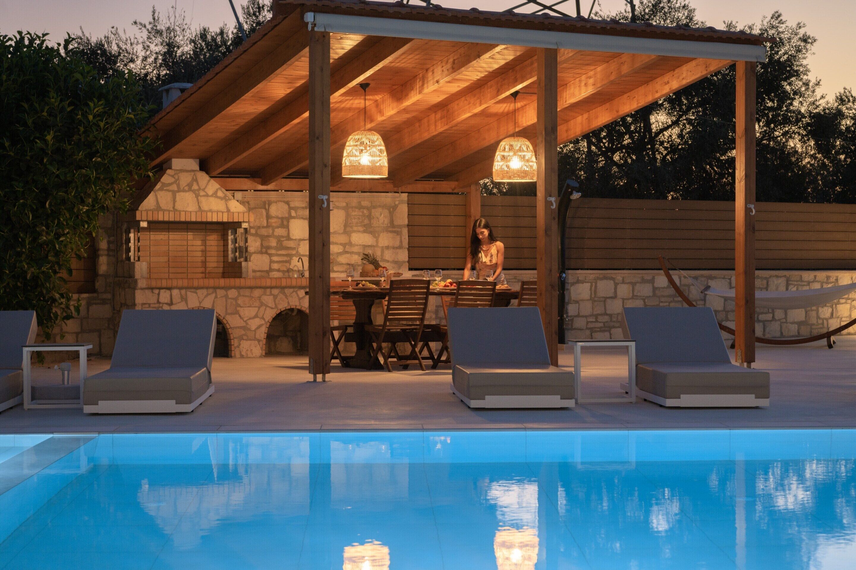 A poolside area with lounge chairs, a stone fireplace, and a covered seating area.