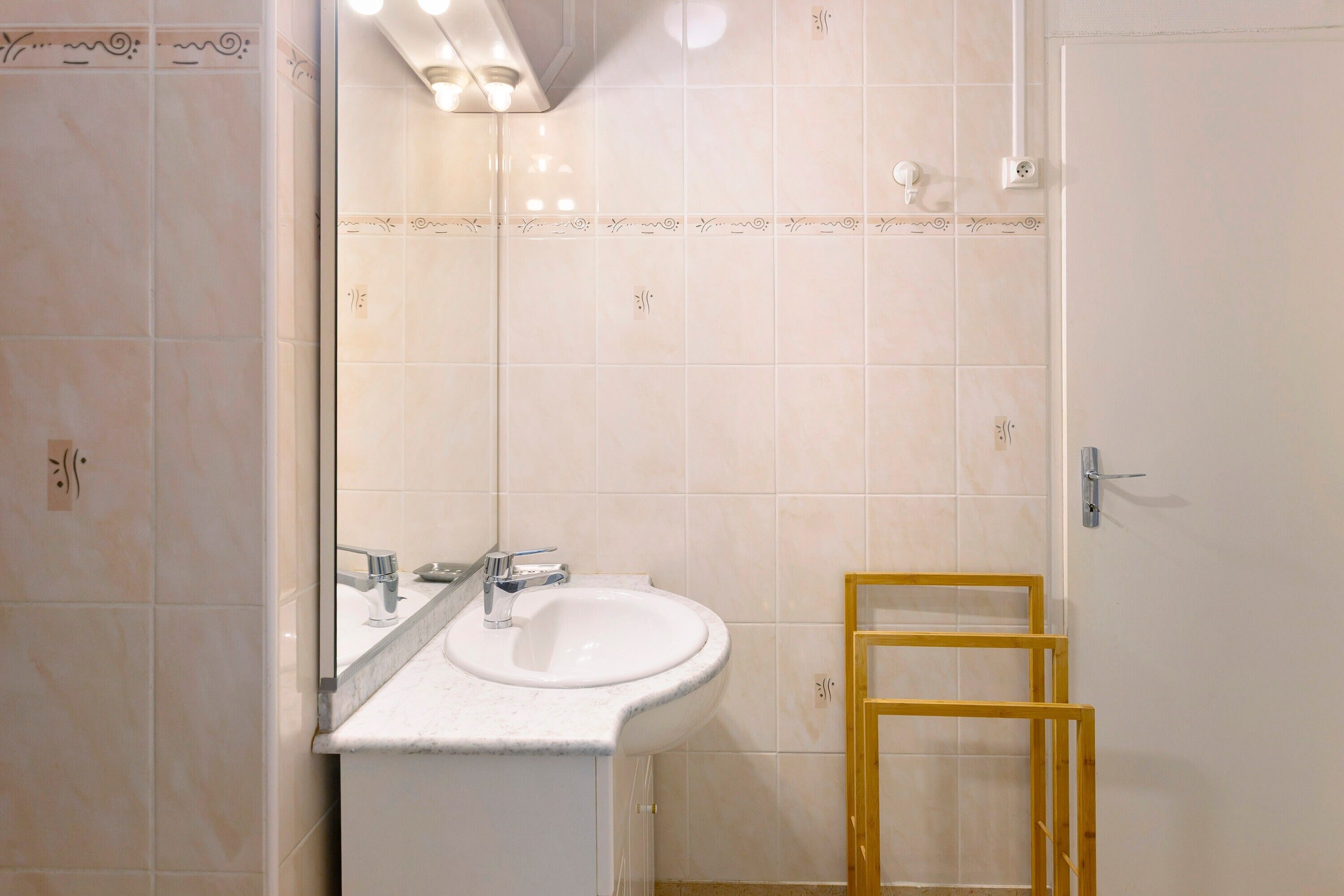 A bathroom with a white sink, a mirror, and a wooden frame leaning against the wall.