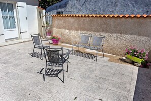 An outdoor patio with a round table and four chairs, a potted plant, and a wall with a textured surface.