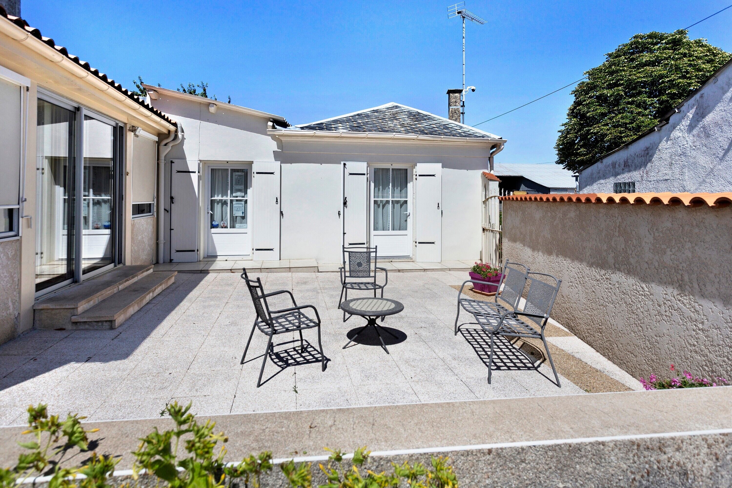 A patio area with a table and chairs, a covered seating area, and a building with a tiled roof and a chimney.