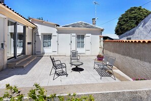Un espace patio avec une table et des chaises, un coin salon abrité et un bâtiment doté d’un toit en tuiles et d’une cheminée.