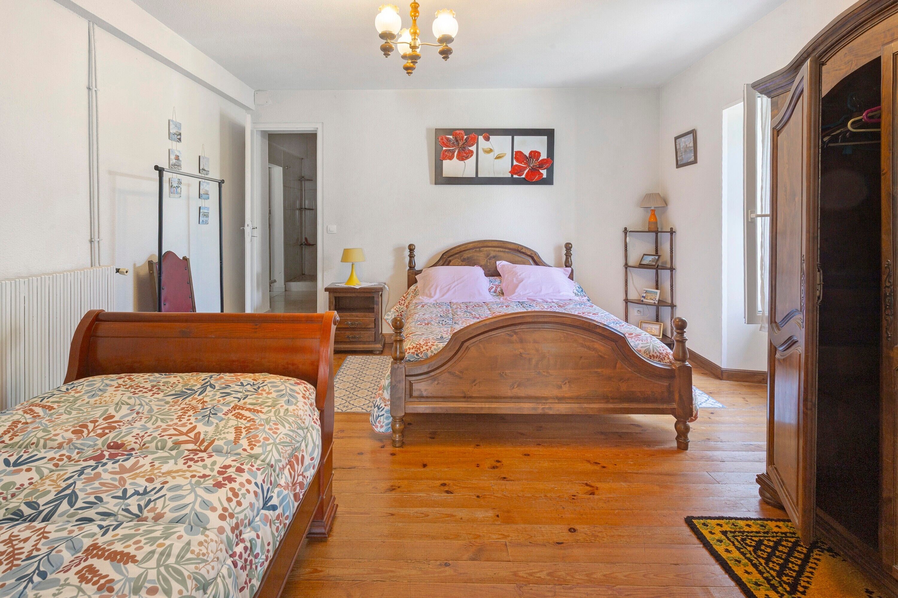 A bedroom with a wooden bed, a bedside table with a lamp, a dresser, and a painting on the wall.