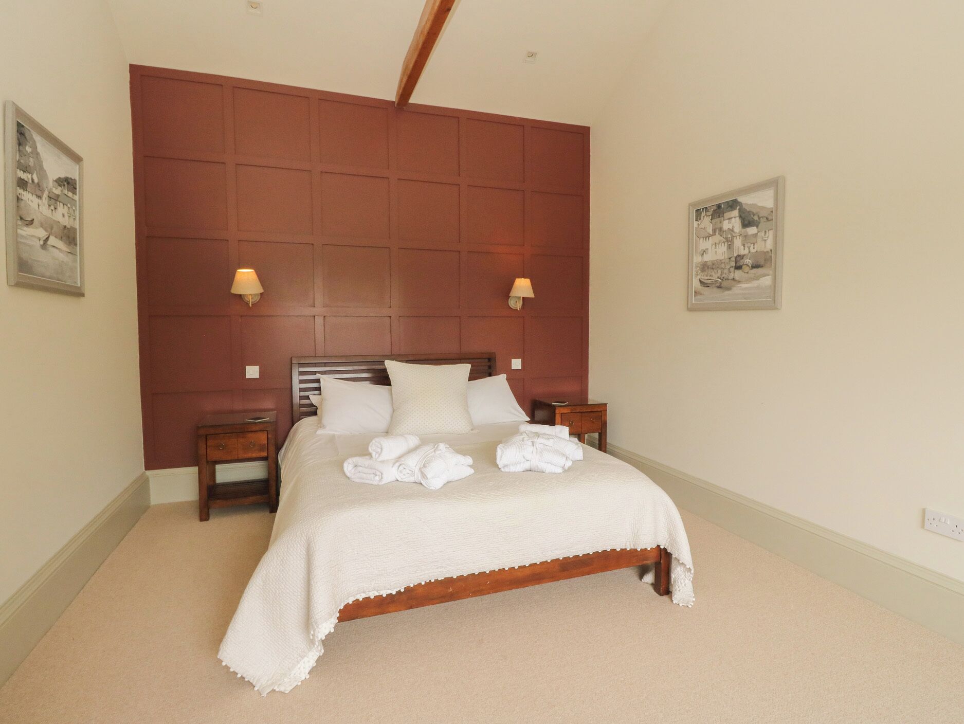 A bedroom with a wooden headboard, a bed with white linens, two bedside tables, and wall-mounted lamps.
