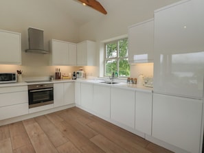 A modern kitchen with white cabinetry, a built-in oven, a microwave, and a window providing a view of greenery outside. - The Tractor Shed (Aberfeldy)