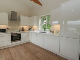 Una cocina moderna con armarios blancos, horno empotrado, microondas y ventana con vistas a zonas verdes.