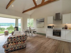A modern kitchen with white cabinets, a built-in oven, and a microwave. There's a dining area with a table and chairs, and a colorful sofa. - The Tractor Shed (Aberfeldy)