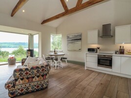 Una cocina moderna con armarios blancos, horno integrado y microondas. Hay una zona de comedor con mesa y sillas, y un sofá de colores.