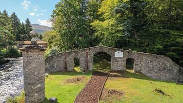 Un puente de piedra con arcos, una zona cubierta de césped y un río al fondo.