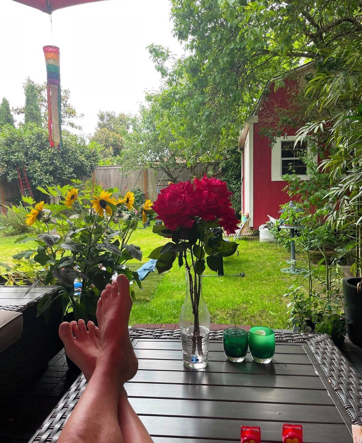A patio with a table, a vase with flowers, and a red building in the background.