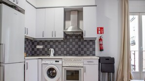 A compact kitchen with a washing machine, oven, and a fire extinguisher on the wall. - 8-guest Malasana Central Suite (Madrid)
