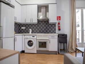 A compact kitchen with a washing machine, oven, and a fire extinguisher on the wall. - 8-guest Malasana Central Suite (Madrid)