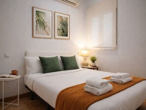 A hotel room with a bed, pillows, a nightstand with a lamp, a small table, and two framed pictures on the wall. - 8-guest Malasana Central Suite (Madrid)