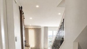 Um interior moderno com piso de madeira, escada com guarda-corpos pretos e vista através de uma grande janela.