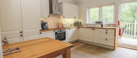 A kitchen with white cabinets, a wooden table, a stove, and a window with a view of greenery.