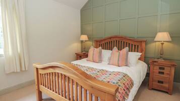A bedroom with a wooden bed, two bedside tables with lamps, a window with curtains, and a green wall paneling.