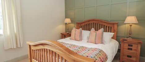 Een slaapkamer met een houten bed, twee nachtkastjes met lampen, een raam met gordijnen en een wandpaneel in groene tinten.