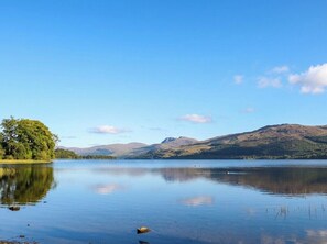 A calm lake with clear reflections, surrounded by hills and a clear sky.