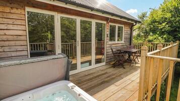 A wooden deck with a hot tub, a covered patio with a table and chairs, and a wooden fence.