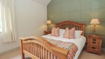 A bedroom with a wooden bed, two bedside tables with lamps, a window with curtains, and a green wall paneling.