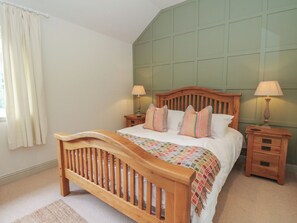 A bedroom with a wooden bed, two bedside tables with lamps, a window with curtains, and a green wall paneling. - Almond (Killin)