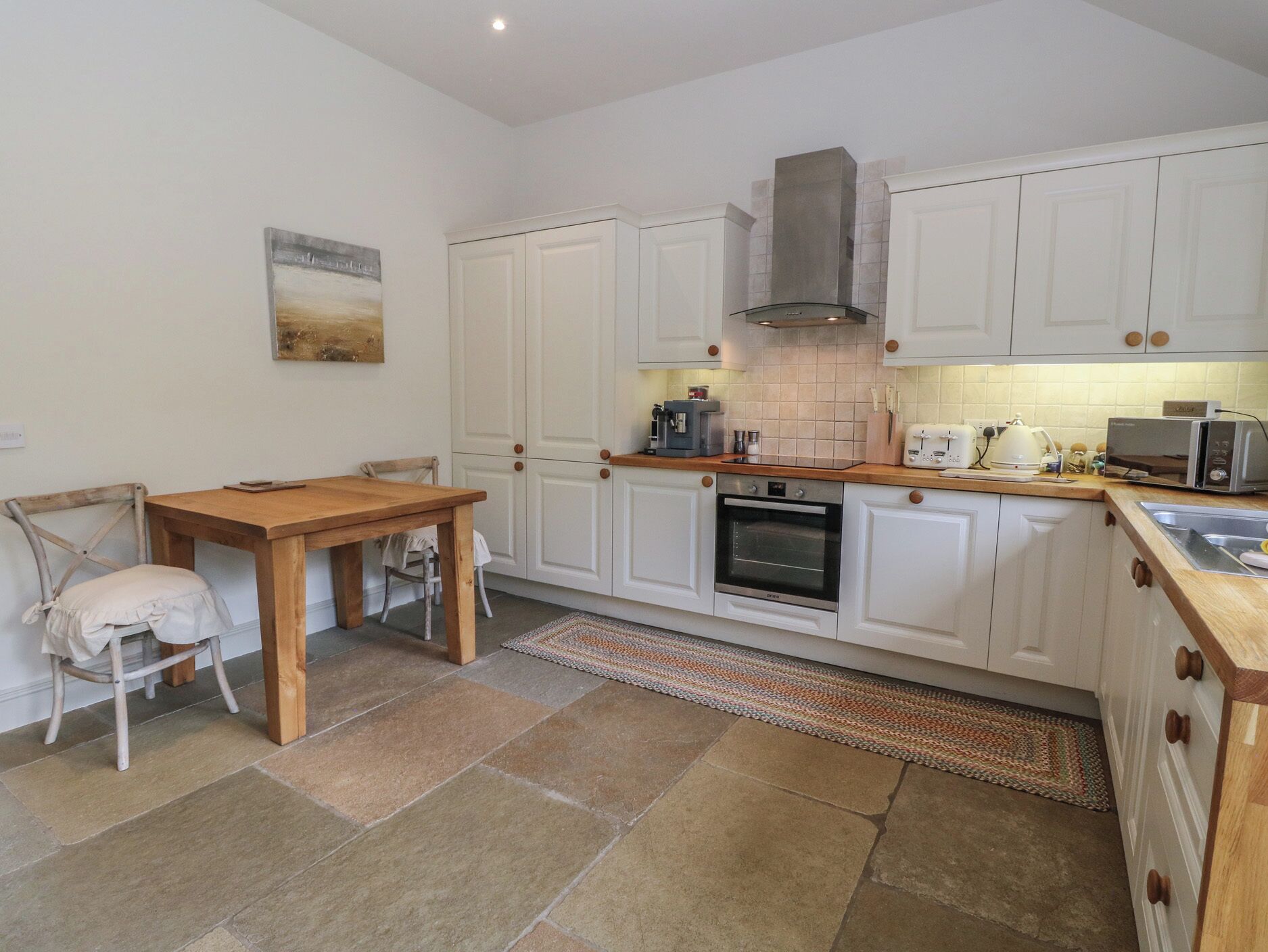 A kitchen with white cabinets, a wooden table, a chair, a stove, and a microwave.