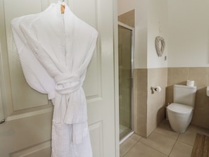 A bathroom with a white bathtub, a glass shower enclosure, a toilet, and a towel rack with a white towel. - Almond (Killin)