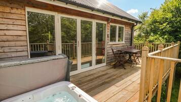 A wooden deck with a hot tub, a wooden table with chairs, and a glass door leading to a covered patio.