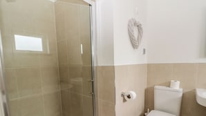 A bathroom with a glass shower enclosure, a toilet, and a sink.