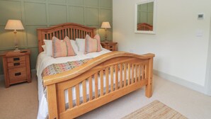 A bedroom with a wooden bed, two bedside tables, a nightstand, a mirror, and a carpeted floor.