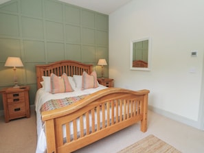 A bedroom with a wooden bed, two bedside tables, a nightstand, a mirror, and a carpeted floor.