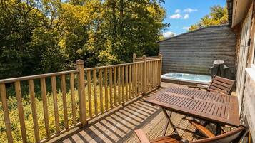 A wooden deck with a table and chairs, a hot tub, and a wooden fence.