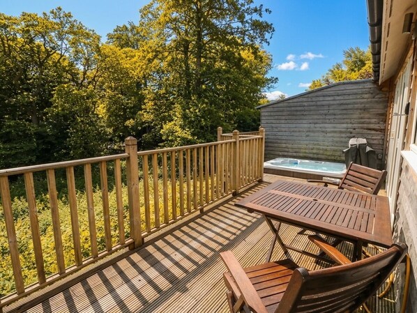 Una terraza de madera con mesa y sillas, un jacuzzi y un cerramiento de madera.