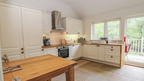 A kitchen with white cabinets, a wooden table, and a window overlooking greenery.