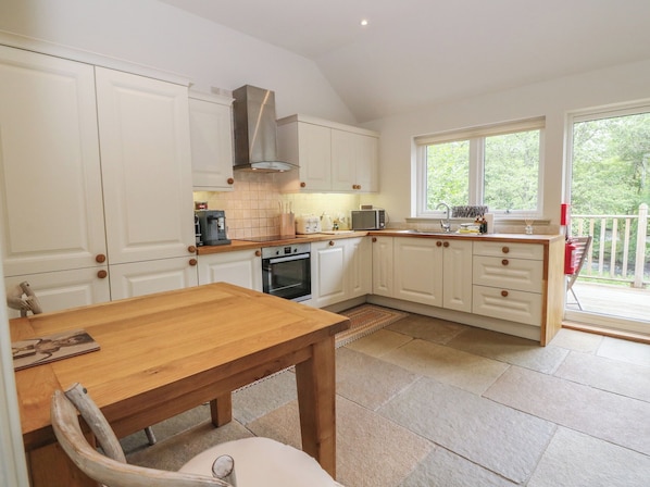 A kitchen with white cabinets, a wooden table, and a window overlooking greenery.