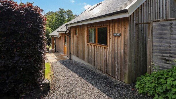 A wooden building with a sloped roof, a gravel pathway, and a sign that reads 'YETT'S'. - Yew Tree (Killin)