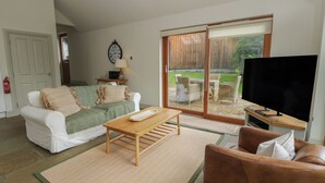 A living room with a sofa, a coffee table, a TV, and a sliding glass door leading to an outdoor patio. - Yew Tree (Killin)