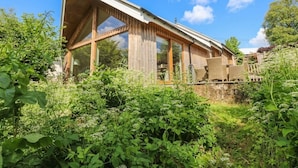 Une maison moderne dotée de grandes fenêtres et d’un toit en pente, entourée d’une végétation luxuriante.