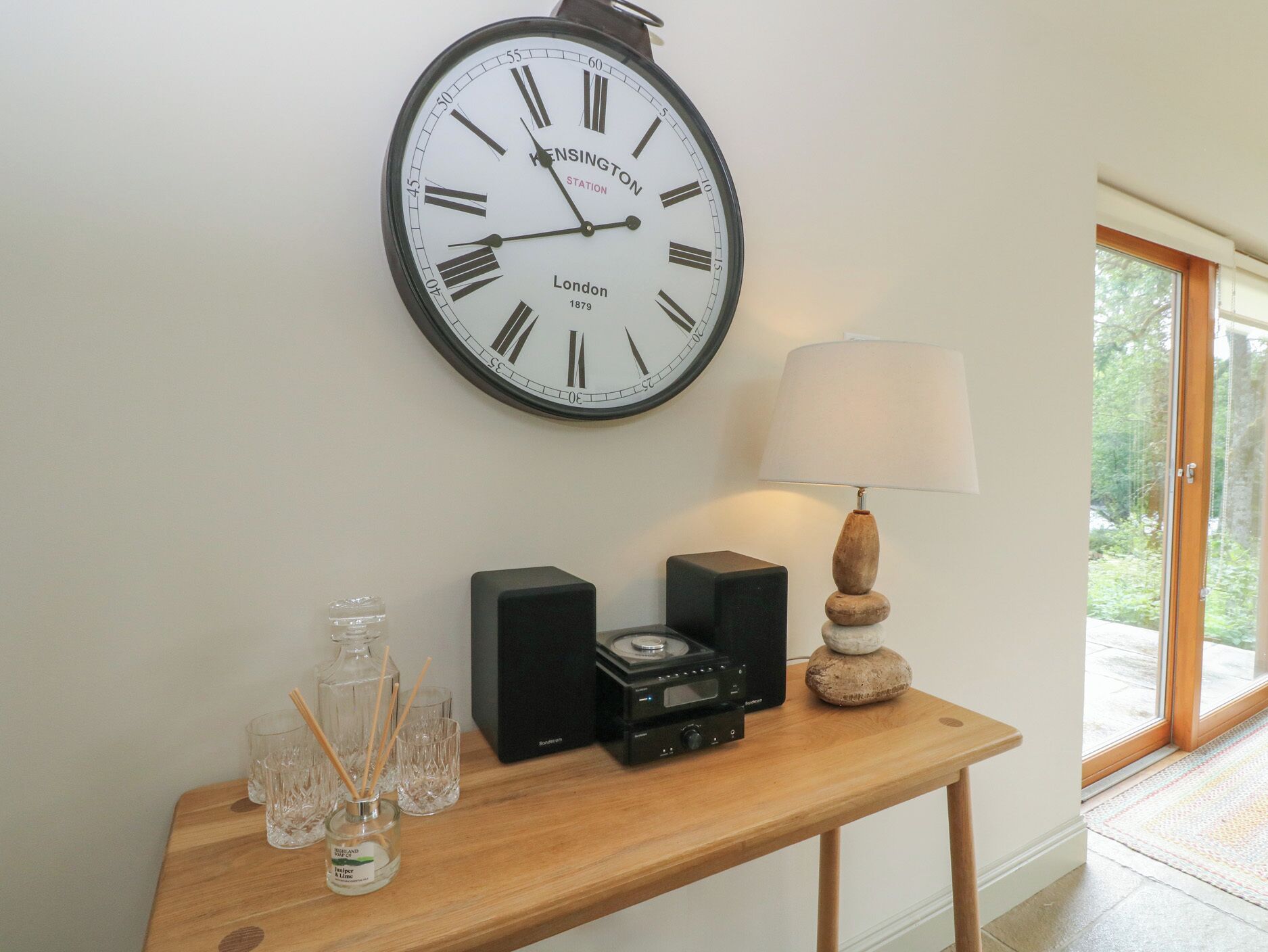 A wall clock with Roman numerals, a table with a lamp, and a speaker.