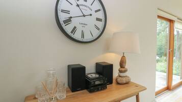 A wall clock with Roman numerals, a table with a lamp, and a speaker.