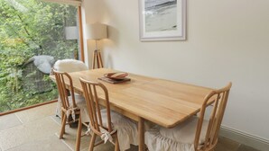 A dining area with a wooden table and chairs, a framed picture on the wall, and a view of greenery outside. - Yew Tree (Killin)