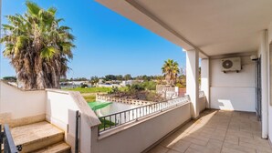 Uma varanda com vista para um gramado verde, palmeiras e uma área residencial.