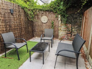 Een terras met vier metalen stoelen en een tafel, omgeven door een bamboescherm en een stenen muur.