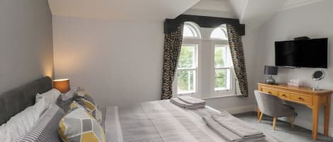 Un dormitorio con cama, escritorio, silla, televisor y ventana con cortinas.