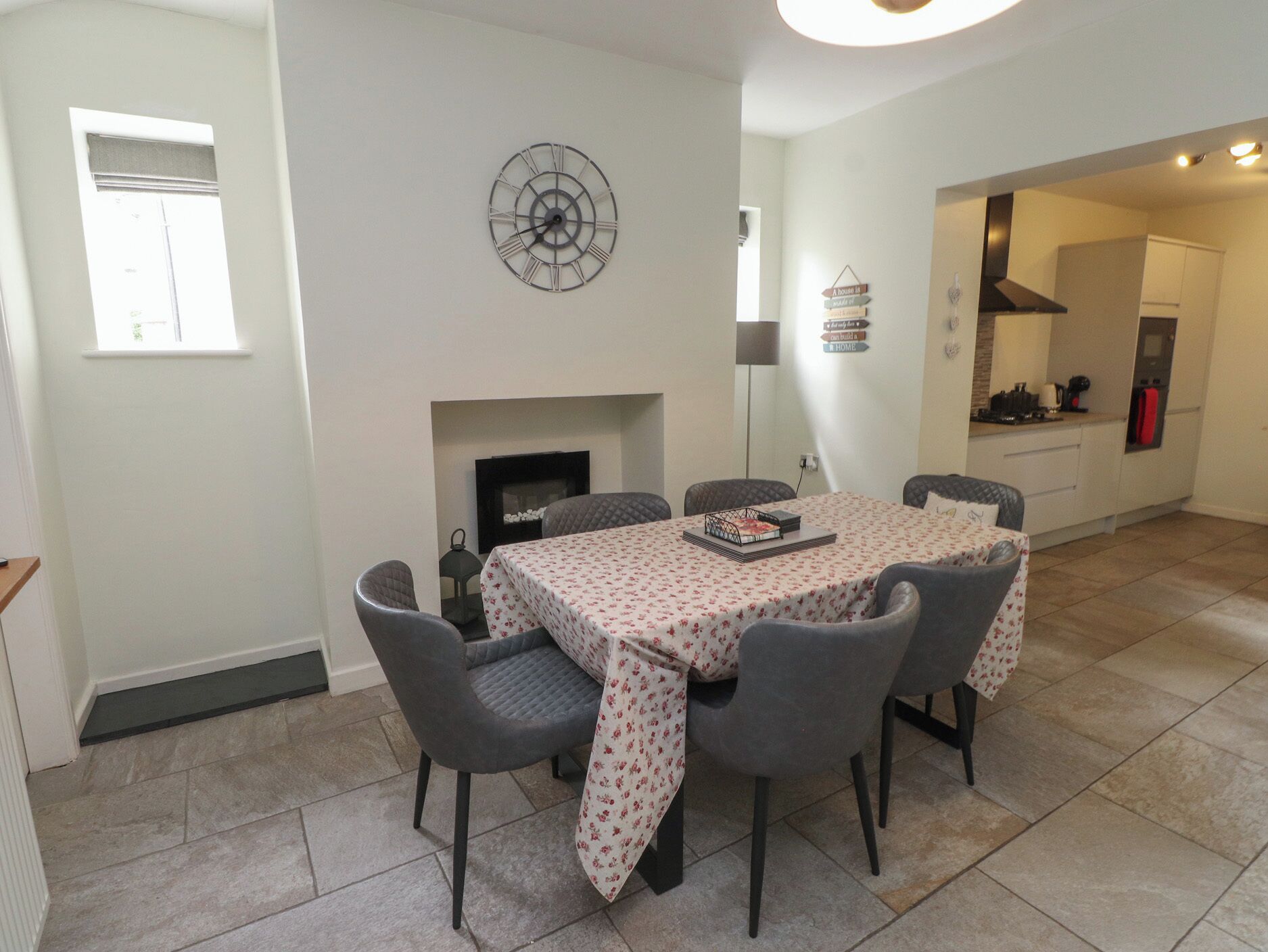Uma sala de jantar com mesa posta para seis pessoas, lareira e um relógio na parede.