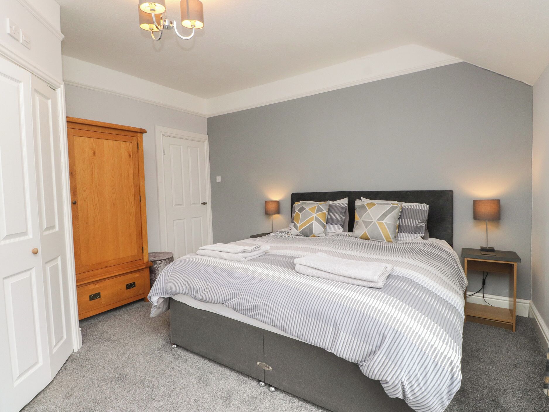 A bedroom with a bed, bedside lamps, a wardrobe, and a door.