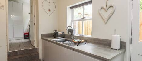 A kitchen with a double sink, a toaster, a window, and a heart-shaped decoration on the wall.