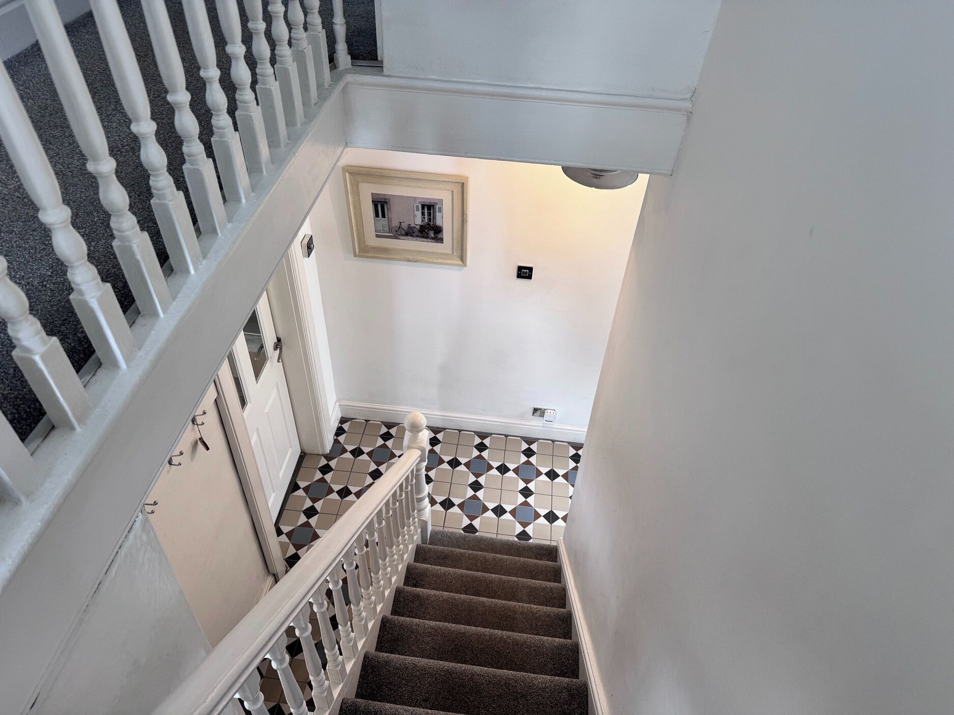 Uma escadaria com corrimão branco, piso estampado e um quadro na parede.