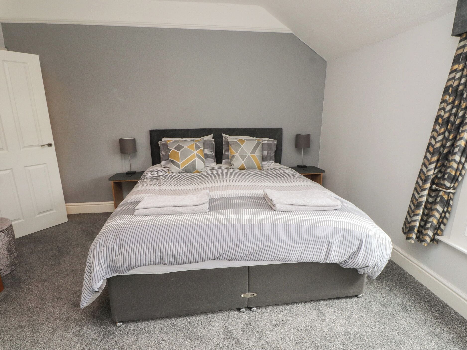 A bedroom with a bed, two bedside tables, a nightstand, a door, and a curtain.