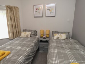 A double room with two beds, a bedside table with lamps, and two framed floral pictures on the wall. - Conway Mart Cottage (Conwy)
